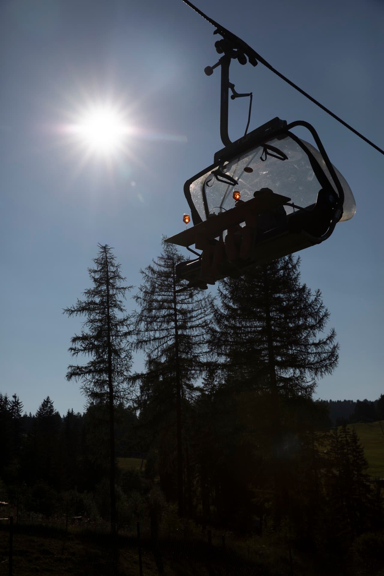 Seggiovia in controluce contro il sole basso, sopra i larici.