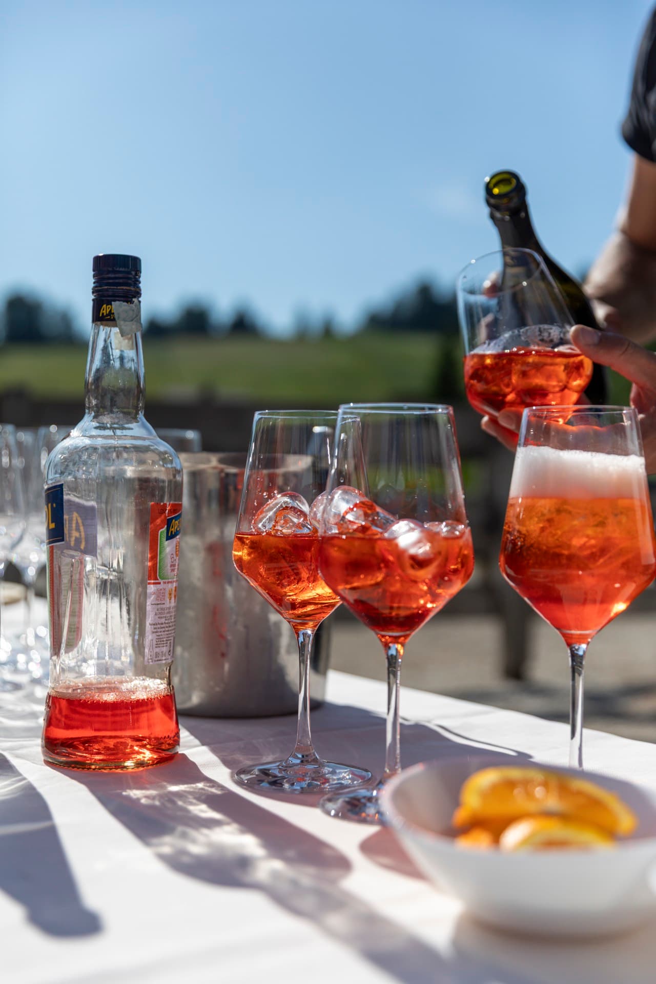 Il barman versa il prosecco nei calici di spritz allineati al sole.